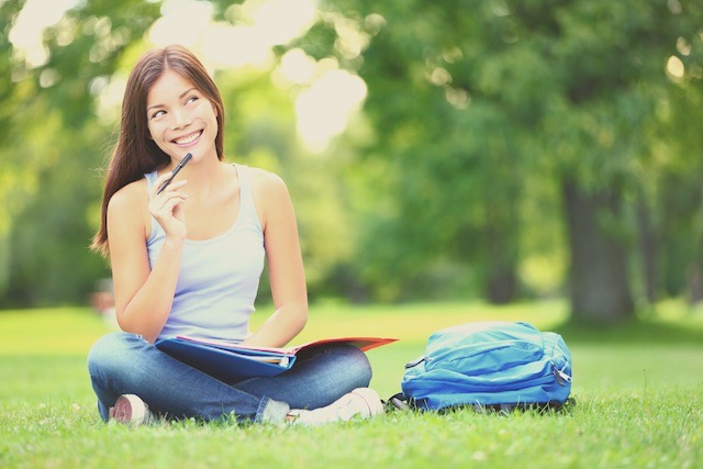 A happy female student is sitting on the grass