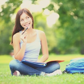 A happy female student is sitting on the grass 